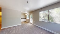 Located at 400 Longbrook Way in Pleasant Hill, California, this single-floor unit offers a well-organized layout with thoughtfully updated finishes throughout. The main living area is generously sized, finished with plush wall-to-wall carpeting and neutral beige walls that create a warm, inviting atmosphere. Multiple windows allow abundant natural light to fill the space, with views of surrounding greenery. A glass panel door opens to the exterior, further connecting the interior to the outdoors. A built-in countertop and white cabinetry nook adds functional storage and workspace at the edge of the living area, where wood-look flooring transitions from the carpeted zones. The kitchen features white shaker-style cabinetry, dark countertops, a stainless steel sink with a modern faucet, and stainless steel appliances including a refrigerator. The bedroom is a quiet, carpeted retreat with a baseboard heater and a window overlooking mature trees. The bathroom is equipped with white tile surround tub and shower combination, a vanity with dark countertop, white cabinetry, and safety grab bars. Wood-look flooring runs through the kitchen and bathroom, tying together the overall clean, updated aesthetic of this well-maintained unit.