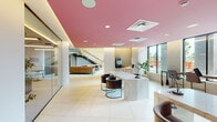 Located at 300 Atlas St in Baltimore, MD, this contemporary lobby showcases a bold and thoughtfully curated design. The space is immediately distinguished by its signature pink ceiling, which spans the entire floor and adds a warm, distinctive character to the interior. Large floor-to-ceiling windows line the perimeter, inviting abundant natural light and offering open views of the surrounding neighborhood streetscape.

The reception area centers around an elegant marble desk accompanied by sleek, dark leather chairs on minimalist metal frames, creating a polished yet approachable focal point. Nearby, a comfortable lounge area features a mix of navy and charcoal sectional sofas, accent chairs in rich cognac leather, and rounded coffee tables arranged atop a light area rug — ideal for casual gatherings or waiting.

A dedicated mail room, clearly marked with bold typographic signage, houses rows of individual brass mailboxes and a central sorting counter with a stone surface. The elevator bank features two elevators framed by refined marble-tiled walls and large-format cream tile flooring consistent throughout the space. An open staircase with a modern metal railing connects to upper levels, adding architectural interest and vertical dimension to the overall design.