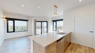 This thoughtfully designed two-bedroom, two-bathroom unit at 112 Webster Street in Dayton, Ohio offers a cohesive modern aesthetic across its single-floor layout. Light wood-style flooring flows consistently throughout, complementing the crisp white walls and creating a bright, clean atmosphere.

The kitchen serves as a focal point of the space, featuring a large center island with quartz countertops, warm wood cabinetry, and brushed gold hardware. Pendant lighting with gold-toned fixtures hangs above the island, and black-framed windows provide ample natural light and urban views. Stainless steel appliances, including a range and refrigerator, complete the functional design. A subtle tile backsplash adds texture behind the range wall.

Both bedrooms feature ceiling fans, light-toned built-in cabinetry for storage, and large windows that invite natural light. The primary bedroom offers a comfortable sense of space, while the second bedroom maintains the same clean, minimalist character.

The two bathrooms are finished with marble-look porcelain tile flooring and white subway tile surrounds. Brushed gold fixtures and hardware carry the unit's warm metallic theme into these rooms. One bathroom includes a glass-enclosed walk-in shower, while the other features a full tub with a frameless sliding glass enclosure.