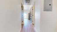 This contemporary single-floor unit showcases a clean, modern design throughout, highlighted by light wood-tone flooring that runs seamlessly across every room. The open hallway welcomes you in with crisp white walls, recessed lighting, and a ceiling-mounted HVAC vent, setting the tone for the bright, well-finished interior.

The kitchen is equipped with stainless steel appliances, including a Samsung electric range and a dishwasher, complemented by sleek grey cabinetry with matte black hardware and a stainless steel countertop with an integrated sink. Open shelving adds a functional, modern touch.

The living area is bathed in natural light streaming through a large floor-to-ceiling sliding glass door that opens to a balcony, offering impressive views of the surrounding cityscape and skyline. Transom windows in additional rooms further enhance the bright, airy atmosphere throughout.

Bedroom spaces feature sliding closet doors with built-in hanging rods, providing practical storage solutions, while the clean white walls offer a neutral, versatile canvas.

The bathroom is thoughtfully designed with a floating vanity, dark countertop, white cabinetry with black hardware, and a backlit square mirror that adds a sophisticated, contemporary accent. A separate water closet provides added privacy and convenience. The overall ambiance of the unit is fresh, modern, and move-in ready.