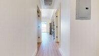 This contemporary single-floor unit showcases a clean, modern design throughout, highlighted by light wood-tone flooring that runs seamlessly across every room. The open hallway welcomes you in with crisp white walls, recessed lighting, and a ceiling-mounted HVAC vent, setting the tone for the bright, well-finished interior.

The kitchen is equipped with stainless steel appliances, including a Samsung electric range and a dishwasher, complemented by sleek grey cabinetry with matte black hardware and a stainless steel countertop with an integrated sink. Open shelving adds a functional, modern touch.

The living area is bathed in natural light streaming through a large floor-to-ceiling sliding glass door that opens to a balcony, offering impressive views of the surrounding cityscape and skyline. Transom windows in additional rooms further enhance the bright, airy atmosphere throughout.

Bedroom spaces feature sliding closet doors with built-in hanging rods, providing practical storage solutions, while the clean white walls offer a neutral, versatile canvas.

The bathroom is thoughtfully designed with a floating vanity, dark countertop, white cabinetry with black hardware, and a backlit square mirror that adds a sophisticated, contemporary accent. A separate water closet provides added privacy and convenience. The overall ambiance of the unit is fresh, modern, and move-in ready.