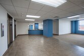 Located at 500 W Pershing Rd in Kansas City, Missouri, this single-floor commercial office space offers a well-organized and functional layout suited for a variety of professional uses. The space is accessed via a lobby area featuring two elevators framed by chrome trim, tiled flooring, and distinctive teal-painted structural columns that serve as a consistent design element throughout the floor.

The open office areas are expansive and carpeted in neutral tones, providing flexible configurations for workstations or collaborative zones. Bold teal accent walls and columns add visual character against the predominantly white walls and drop tile ceilings illuminated by recessed fluorescent panel lighting. Structural columns are thoughtfully integrated throughout, defining zones without fully enclosing them.

Private offices line the perimeter, several of which feature windows overlooking the surrounding Kansas City urban landscape, allowing natural light to filter into the space. Warm wood-trimmed doors with sidelight glass panels contribute a professional aesthetic throughout the corridors and office entries.

A dedicated kitchenette provides ample cabinetry, extended countertops, a sink, and a dishwasher, making it well-equipped for daily staff use. Long corridors connect the various sections of the floor, creating a logical and navigable flow. Overall, the space presents a clean, ready-to-occupy commercial environment with practical amenities and a cohesive design identity.