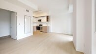 This contemporary 2-bedroom, 1-bathroom residence offers a thoughtfully designed layout spread across a well-utilized floor plan. Light-toned hardwood flooring runs throughout, complementing the bright, minimalist aesthetic defined by crisp white walls and clean architectural lines.

The open-concept living and dining area is a standout feature, bathed in natural light through expansive floor-to-ceiling windows that frame views of the surrounding urban landscape. A sleek kitchen is integrated into the living space, outfitted with stainless steel appliances — including a range, microwave, and dishwasher — alongside two-tone cabinetry with open shelving and track lighting above.

A wood-railed staircase connects to the upper level, where a private outdoor terrace is accessible through large sliding glass doors, offering additional outdoor living space with city views. Both bedrooms are well-proportioned and bright, each benefiting from generous window coverage and access to natural light. The primary bedroom includes a built-in sliding door closet. The full bathroom features a soaker tub with a tiled surround, a wood-fronted vanity, and light tile flooring. A dedicated in-unit laundry closet with a stacked washer and dryer adds everyday convenience to this efficiently designed urban home.