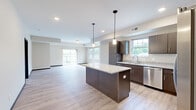 This well-appointed 3-bedroom, 2-bathroom home in Red Wing, Minnesota offers a thoughtfully designed single-level layout with modern finishes throughout. The open-concept kitchen and living area serves as the heart of the home, featuring rich dark-wood cabinetry, granite countertops, a central island with pendant lighting, and a full suite of stainless steel appliances. Light-toned luxury vinyl plank flooring flows seamlessly through the main living areas, complementing the bright, neutral color palette. The spacious living room benefits from large sliding glass doors that open to a private balcony, filling the space with natural light and offering pleasant outdoor views. A hallway connects the living areas to the private quarters, where three carpeted bedrooms provide comfortable retreats. The generously sized primary bedroom includes a ceiling fan and a dedicated closet. Each bathroom is finished with granite-topped dark wood vanities, undermount sinks, and stylish hexagonal tile flooring, with a tall linen cabinet for added storage. Three closets throughout the home offer ample organization space. A dedicated in-unit laundry room with full-size washer and dryer adds everyday convenience. The clean, contemporary aesthetic and functional layout make this a comfortable and practical home.