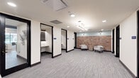 Located at 1300 Front Ave in Columbus, Georgia, this thoughtfully designed professional office suite offers a well-appointed single-floor layout that balances collaborative and private workspaces. The open central corridor is finished with neutral-toned patterned carpet and recessed lighting, creating a clean, polished atmosphere throughout.

Several enclosed micro-offices line the space, each featuring a built-in desk with under-shelf LED accent lighting, a perforated panel backdrop, and glass-panel doors with black frames — ideal for focused, individual work. The suite also includes a dedicated conference room that serves as a standout feature, appointed with a round walnut table, modern ergonomic seating, textured wood-panel wall accents, and a striking sputnik chandelier. A wall-mounted display screen and soft blue-gray walls complete the room's refined, contemporary aesthetic.

The open lounge area offers a welcoming seating arrangement with white upholstered chairs set against a warm terracotta tile accent wall, illuminated by a decorative multi-arm light fixture. Additional storage and greenery add character to another wall featuring a white brick accent. Three bathrooms serve the suite, ensuring full functionality. The overall design blends modern professionalism with warm, carefully curated finishes throughout.