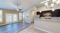 Located at 1006 Cider Mill Loop in Weaverville, NC, this well-appointed 2-bedroom, 2-bathroom single-story home offers a thoughtfully designed open-concept layout with modern finishes throughout. The combined living, dining, and kitchen area serves as the heart of the home, featuring soaring vaulted ceilings, a ceiling fan, and a chandelier over the dining space. The kitchen is equipped with dark espresso cabinetry, granite countertops, stainless steel appliances, pendant lighting, and a peninsula island — all set on clean tile flooring that transitions seamlessly into wood-look flooring in the living areas. Natural light flows generously through multiple windows fitted with blinds. Both bedrooms feature the same wood-look flooring, neutral tones, and windows with outdoor views, while the spacious primary bedroom includes its own dedicated closet. The bathrooms are finished with granite-topped dark vanities and tile flooring. A dedicated laundry room with built-in shelving and utility hookups adds everyday convenience. Each bedroom is complemented by a well-sized closet with wire shelving. The overall ambiance is clean, bright, and move-in ready, with a consistent neutral palette and quality finishes throughout.