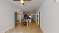 This single-floor residence is designed with a clean, contemporary aesthetic throughout. The open-concept layout connects the living, dining, and kitchen areas into one cohesive space, finished with light hardwood-style flooring and crisp white walls accented by crown molding. Ceiling fans in both the living area and bedroom provide additional comfort.

The kitchen is a standout feature, offering an expansive peninsula with a white quartz countertop that doubles as a breakfast bar. Gray shaker-style cabinetry extends to the ceiling, providing ample storage, while stainless steel appliances—including a French door refrigerator with ice maker, a range, and a built-in microwave—complete the well-appointed space. Pendant lighting above the peninsula adds a warm, functional glow.

Adjacent to the kitchen, a dedicated dining area accommodates a full dining table with ease. A conveniently located in-unit washer is tucked into a side alcove, adding practical functionality.

The bathroom features a gray vanity with a white countertop, a large mirror, and a tiled shower-tub combination. The bedroom is carpeted, benefits from natural light through a sizable window with blinds, and includes a ceiling fan.