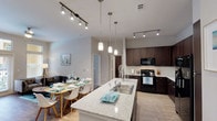 This well-appointed single-floor residence showcases a thoughtfully designed open-concept layout that seamlessly connects the kitchen, dining, and living areas. The kitchen is a standout feature, boasting rich dark-espresso cabinetry, granite-style countertops, a large center island with a stainless steel sink, pendant lighting, and a full suite of black appliances including a refrigerator with ice maker, electric range, and built-in microwave. A white subway tile backsplash adds a clean, modern contrast. Track lighting runs throughout the kitchen and dining area, enhancing both functionality and ambiance. The living room is bright and welcoming, with French doors topped by transom windows that open to a private balcony, flooding the space with natural light. Wood-look flooring and a ceiling fan complete the comfortable atmosphere. A dedicated in-unit laundry area provides added convenience. The primary bedroom features plush carpeting, a ceiling fan, and a large window with outdoor views, while its en-suite bathroom offers granite countertops, a walk-in shower, and dark cabinetry. The second bedroom is equally comfortable, and the second full bathroom includes a tub-shower combination with tile surround.