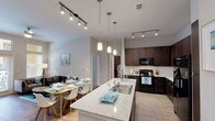 This well-appointed single-floor residence showcases a thoughtfully designed open-concept layout that seamlessly connects the kitchen, dining, and living areas. The kitchen is a standout feature, boasting rich dark-espresso cabinetry, granite-style countertops, a large center island with a stainless steel sink, pendant lighting, and a full suite of black appliances including a refrigerator with ice maker, electric range, and built-in microwave. A white subway tile backsplash adds a clean, modern contrast. Track lighting runs throughout the kitchen and dining area, enhancing both functionality and ambiance. The living room is bright and welcoming, with French doors topped by transom windows that open to a private balcony, flooding the space with natural light. Wood-look flooring and a ceiling fan complete the comfortable atmosphere. A dedicated in-unit laundry area provides added convenience. The primary bedroom features plush carpeting, a ceiling fan, and a large window with outdoor views, while its en-suite bathroom offers granite countertops, a walk-in shower, and dark cabinetry. The second bedroom is equally comfortable, and the second full bathroom includes a tub-shower combination with tile surround.