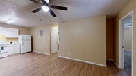 This single-floor unit is designed with a practical, straightforward layout that flows between clearly defined living spaces. The main living area features light wood-look laminate flooring, warm beige walls, and a textured ceiling with a ceiling fan overhead. A wall-mounted electrical panel and a window-unit air conditioner are notable functional features. Natural light enters through a window near the front entry door, brightening the space.

The kitchen is laid out in an L-shape and is well-equipped with ample white cabinetry both above and below the countertops, a double-basin sink, a white electric range, a dishwasher, and a full-size refrigerator. A track lighting fixture illuminates the workspace, and the same wood-look flooring continues throughout.

The bedrooms are carpeted and include ceiling fans. One bedroom features a walk-in closet, while another offers access to a spacious closet room and an additional adjoining space. The bathroom includes a vanity with a speckled countertop, white cabinetry, a toilet, and a tub-shower combination. Throughout, the consistent warm beige palette and textured ceilings provide a cohesive, understated aesthetic.