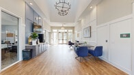 This single-story community clubhouse is thoughtfully designed to offer residents a comprehensive amenity experience. The expansive main lobby greets visitors with soaring ceilings, warm hardwood-style flooring, and an eye-catching multi-tier chandelier. Wainscoting panels line the walls, while large French doors flood the space with natural light and provide direct access to the outdoor pool area. Comfortable blue lounge seating and collaborative tables make the lobby an inviting gathering space.

Adjacent to the lobby, a built-in service counter with gray cabinetry and a wall-mounted TV anchors a stylish lounge area, complemented by curated artwork and accent lighting. A separate seating nook features teal dining chairs around a round table, adding a relaxed social zone. The kitchenette is well-equipped with quartz countertops, a subway tile backsplash, open shelving, a stainless steel refrigerator, microwave, and a matte black faucet.

The fitness center is a standout feature, boasting exposed wood beam ceiling details, light blue accent walls, and floor-to-ceiling windows that bathe the space in natural light. It is outfitted with treadmills, free weights, resistance equipment, and wall mirrors. Private office or meeting rooms with glass-panel doors round out this versatile and amenity-rich facility.