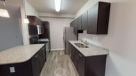 This single-floor residence at Ashby Green offers a well-designed, open-concept layout that balances modern aesthetics with everyday functionality. The living area is generously proportioned, featuring warm wood-look plank flooring, a ceiling fan with light fixture, and a set of French doors that invite natural light and provide access to the outdoors. The space flows seamlessly into the kitchen, which is equipped with dark espresso cabinetry, granite-look countertops, a full suite of stainless steel appliances including a refrigerator, electric range, built-in microwave, and dishwasher, as well as a double-basin sink. A breakfast bar with pendant lighting connects the kitchen to the living area, enhancing the open feel. The bedrooms are carpeted for comfort, each with ceiling fans and windows with blinds that allow for natural light and privacy. The bathroom is finished with wood-look vinyl flooring, a dark vanity with granite-look countertop, and a full tub-shower combination. Neutral tones throughout the home create a clean, cohesive aesthetic that is both inviting and move-in ready.