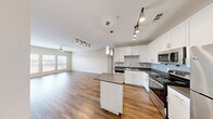 Located at 1215 E Owassa Rd in Edinburg, TX, this single-story 2-bedroom, 2-bathroom home offers a well-designed layout with a clean, modern aesthetic throughout. The open-concept living room and kitchen area serves as the heart of the home, featuring rich hardwood-style flooring, neutral warm-toned walls, and abundant natural light streaming through multiple windows fitted with blinds. A ceiling fan anchors the living space, adding both function and style.

The kitchen is thoughtfully appointed with white shaker-style cabinetry, subway tile backsplash, dark countertops, and a full suite of stainless steel appliances including a refrigerator, range, microwave, and dishwasher. A center island with pendant lighting and an additional track light fixture provide ample workspace and a contemporary feel.

Both bedrooms are carpeted in a neutral tan tone, offering comfort underfoot, and each features a ceiling fan and windows that invite natural light. The primary bedroom provides a generous, well-proportioned space.

The two bathrooms are finished with tile flooring, white vanity cabinets, dark countertops, framed mirrors, and tub-shower combinations clad in classic white subway tile. A connecting hallway ties the layout together efficiently, creating a cohesive and functional living environment.
