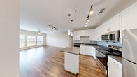 Located at 1215 E Owassa Rd in Edinburg, TX, this single-story 2-bedroom, 2-bathroom home offers a well-designed layout with a clean, modern aesthetic throughout. The open-concept living room and kitchen area serves as the heart of the home, featuring rich hardwood-style flooring, neutral warm-toned walls, and abundant natural light streaming through multiple windows fitted with blinds. A ceiling fan anchors the living space, adding both function and style.

The kitchen is thoughtfully appointed with white shaker-style cabinetry, subway tile backsplash, dark countertops, and a full suite of stainless steel appliances including a refrigerator, range, microwave, and dishwasher. A center island with pendant lighting and an additional track light fixture provide ample workspace and a contemporary feel.

Both bedrooms are carpeted in a neutral tan tone, offering comfort underfoot, and each features a ceiling fan and windows that invite natural light. The primary bedroom provides a generous, well-proportioned space.

The two bathrooms are finished with tile flooring, white vanity cabinets, dark countertops, framed mirrors, and tub-shower combinations clad in classic white subway tile. A connecting hallway ties the layout together efficiently, creating a cohesive and functional living environment.