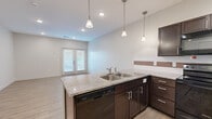 This single-floor residence offers a thoughtfully designed layout that balances function and comfort throughout. The kitchen serves as a central highlight, showcasing rich dark-espresso cabinetry with brushed nickel hardware, granite countertops, and a full suite of black appliances including a range, over-the-range microwave, dishwasher, and refrigerator. A decorative tile backsplash adds visual interest, while pendant lighting suspended from the ceiling enhances the space with warm, focused illumination. The kitchen flows naturally into an open living and dining area finished with wood-look tile flooring, recessed lighting, and sliding glass doors that invite natural light and provide outdoor access. The bedrooms are carpeted for comfort and each features a double-door closet for generous storage. A connecting hallway links the private areas of the residence seamlessly. Two full bathrooms are finished with matching dark vanity cabinetry, white countertops, and hexagonal tile flooring. The primary bathroom includes a soaking tub with shower combination and built-in shelving, while the secondary bathroom offers a single vanity with ample storage. Neutral wall tones and clean architectural lines throughout contribute to a bright, modern ambiance well-suited for everyday living.