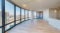 Located in Chicago's River North neighborhood at 520 N Kingsbury Street, this high-rise unit offers a compelling blend of modern design and sweeping urban panoramas. The open-concept living area is defined by a dramatic curved wall of floor-to-ceiling windows, flooding the space with natural light and framing breathtaking views of the Chicago skyline and surrounding cityscape. Light hardwood flooring flows throughout, complementing the clean, contemporary aesthetic. A balcony access door in the main living area extends the connection to the outdoors. The kitchen is thoughtfully designed with light wood cabinetry, a white tile backsplash, quartz countertops, and a full suite of stainless steel appliances, including a refrigerator, dishwasher, and range. A dedicated bedroom offers generous proportions, large windows with city views, and access to a spacious walk-in closet outfitted with wire shelving and hanging rods. A secondary room provides flexible use as a bedroom or office, with its own window overlooking the city. The full bathroom features a double-sink vanity with a white quartz countertop, wood cabinetry, a large wall mirror, and a shower/tub combination, finished with neutral tile flooring throughout.