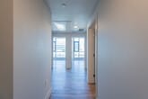 This contemporary single-floor residence offers a clean, modern aesthetic defined by light wood-look flooring, crisp white walls, and an abundance of natural light. A wide hallway with smooth ceilings leads into the open living areas, setting a bright and airy tone throughout.

The kitchen is thoughtfully designed with a two-tone cabinetry scheme — warm wood lower cabinets paired with high-gloss white uppers — complemented by a textured gray subway tile backsplash and light quartz countertops. Stainless steel appliances, including a gas range, over-range microwave, and French door refrigerator, complete this functional and stylish space.

The living and bedroom areas benefit from expansive floor-to-ceiling windows framed in black, delivering sweeping urban views of the surrounding cityscape and filling the rooms with natural light. The spacious layout provides a comfortable, open feel.

Two bathrooms reflect a consistent modern design language, each finished with gray subway tile. One features a soaking tub with a shower combination, while the other offers a walk-in glass-enclosed shower. Both include wood-look flooring for a cohesive look.

A dedicated in-unit laundry area houses a stacked GE washer and dryer, adding practical convenience. Overall, this residence presents a polished, contemporary living environment with urban energy and refined finishes throughout.