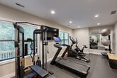 Located at 1021 Ashland Rd in Columbia, Missouri, this dedicated exercise room is a thoughtfully designed private fitness space that offers a comprehensive workout environment. The room is finished with durable grey carpet flooring suited for athletic use, neutral-toned walls, and recessed lighting throughout the ceiling, creating a clean and focused atmosphere.

The space is equipped with a strong selection of cardio and strength training equipment, including a treadmill with an integrated touchscreen display, an elliptical trainer, a stationary cycle, and a cable resistance machine by CENTR. A full dumbbell rack with a range of weights and an adjustable workout bench provide ample options for free weight training. A wall-mounted flat-screen television enhances the workout experience, while stability balls and balance accessories round out the available equipment.

A large wall mirror runs along one end of the room, visually expanding the space and allowing for form monitoring during exercise. Multiple windows fitted with blinds bring in natural light while maintaining privacy. The room is accessed through a frosted-glass interior door, offering a defined separation from the rest of the property. Overall, this exercise room is a fully functional, private fitness facility designed to support a wide range of training routines.