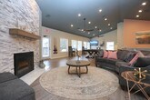This single-floor community clubhouse offers a well-appointed and inviting gathering space designed for both relaxation and social interaction. The open-concept main area features warm luxury vinyl plank flooring throughout, dramatic dark ceilings with recessed and pendant lighting, and soaring vaulted walls that lend a sense of spaciousness and height.

The lounge area is anchored by plush seating arranged around a central rug, creating a comfortable social hub. A striking floor-to-ceiling stacked stone fireplace with a rustic wood mantel serves as a prominent architectural focal point, adding warmth and character to the space. Adjacent to the lounge, a dedicated game area includes a full-size pool table with wall-mounted cue storage and windows that invite natural light.

A built-in coffee bar with a marble-style countertop and bar seating provides a functional café-style amenity. Nearby, a welcoming reception nook with a chalkboard sign and two accent chairs leads into a glass-paneled private office, ideal for leasing or administrative use. Additional seating areas and colorful wall art are distributed throughout, contributing to the space's modern yet approachable aesthetic. Multiple windows and glass doors connect the interior to the outdoors, enhancing the bright, airy atmosphere.