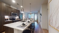 This single-floor residence showcases a thoughtfully designed open-concept layout that seamlessly connects the kitchen, dining, and living areas. The kitchen is a standout feature, equipped with stainless steel appliances including a side-by-side refrigerator, electric range, microwave, and dishwasher. Rich dark wood cabinetry extends to the ceiling, providing ample storage, while crisp white quartz countertops offer generous prep space. A large central island with an undermount sink doubles as a casual dining bar, complemented by sleek pendant lighting overhead. Light wood-tone flooring runs throughout the main living areas, enhancing the bright, airy atmosphere.

The living room benefits from large windows dressed with blinds and sheer curtains, allowing abundant natural light to fill the space. The bedrooms continue the light and airy feel, featuring plush carpeting, ceiling fans, and generously sized windows with outdoor views of lush greenery. The bathroom is finished with a dark wood vanity, white countertop, and wood-look flooring, with direct access to a walk-in closet. Throughout the residence, clean white walls, recessed lighting, and cohesive modern finishes create a polished, contemporary ambiance.