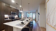 This single-floor residence showcases a thoughtfully designed open-concept layout that seamlessly connects the kitchen, dining, and living areas. The kitchen is a standout feature, equipped with stainless steel appliances including a side-by-side refrigerator, electric range, microwave, and dishwasher. Rich dark wood cabinetry extends to the ceiling, providing ample storage, while crisp white quartz countertops offer generous prep space. A large central island with an undermount sink doubles as a casual dining bar, complemented by sleek pendant lighting overhead. Light wood-tone flooring runs throughout the main living areas, enhancing the bright, airy atmosphere.

The living room benefits from large windows dressed with blinds and sheer curtains, allowing abundant natural light to fill the space. The bedrooms continue the light and airy feel, featuring plush carpeting, ceiling fans, and generously sized windows with outdoor views of lush greenery. The bathroom is finished with a dark wood vanity, white countertop, and wood-look flooring, with direct access to a walk-in closet. Throughout the residence, clean white walls, recessed lighting, and cohesive modern finishes create a polished, contemporary ambiance.