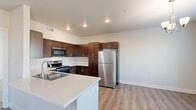This single-floor residence offers a functional and modern layout across two bedrooms, three bathrooms, and a well-organized collection of living spaces. The kitchen is a standout feature, showcasing rich dark wood cabinetry, stainless steel appliances including a refrigerator, microwave, and range, and a light-toned countertop island with an integrated sink — all set atop durable wood-look flooring. Recessed lighting adds a clean, contemporary feel to the kitchen and adjoining areas.

The living room benefits from natural light streaming through horizontal-blind windows and a glass-panel door that opens to an outdoor area, complemented by a ceiling fan overhead and warm hardwood-style flooring throughout.

Both bedrooms are carpeted and feature ceiling fans. The primary bedroom includes access to a dedicated closet and connects to an en suite bathroom with a long vanity, dark cabinetry, a large mirror, and a textured glass-enclosed shower. A second bathroom provides a tub-shower combination with clean white surroundings and wood-look flooring.

A dedicated laundry area with a washer, shelving, and adjacent storage adds everyday convenience. Three hallways connect the spaces efficiently, while two closets offer generous storage throughout this well-designed residence.