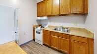 Located at 2100 Greentree North in Clarksville, Indiana, this one-bedroom, one-bathroom unit offers a practical and well-organized layout across a single floor. The living area is bright and open, featuring wood-look laminate flooring, neutral light-gray walls, and a textured ceiling. A window allows natural light to fill the space, complemented by a wall-mounted HVAC unit for year-round comfort.

The kitchen is equipped with warm honey-toned wood cabinetry offering ample upper and lower storage, light laminate countertops, a stainless steel sink, and a white electric range with overhead ventilation. The flooring continues seamlessly from the living area, maintaining a cohesive look throughout.

The bedroom is a comfortable, well-proportioned room with its own window providing natural light and outdoor views. A built-in closet with open shelving and a sliding wood-panel door provides convenient storage. Warm-toned wood doors connect to the hallway, bathroom, and closet areas, adding a classic touch.

The bathroom features a full tub-shower combination with white square tile surround, stainless steel grab bars for added accessibility and safety, and a standard toilet. The hallway connects all rooms efficiently, completing the functional flow of this compact yet complete residence.