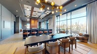 Located in Chicago's vibrant West Loop neighborhood, this elegantly designed communal space spans a single open floor and offers a seamless blend of function and refined aesthetics. The layout flows naturally between three distinct zones: a fully equipped kitchen, a formal dining area, and a comfortable lounge.

The kitchen is outfitted with dark cabinetry, matte black countertops with brass fixtures, dual undermount sinks, and a striking geometric-patterned tile floor that adds a bold design statement. A glowing amber-tiled accent wall and warmly lit pendant fixtures lend the kitchen a sophisticated, editorial quality.

The dining area centers around a large dark communal table surrounded by curved upholstered chairs, anchored by a patterned area rug. Overhead, a dramatic brass sputnik-style chandelier with globe lights draws the eye upward toward a coffered ceiling with inset panels, reinforcing the space's architectural depth.

The lounge area features a generous sectional sofa positioned to take full advantage of floor-to-ceiling glass walls and doors that open to an outdoor terrace, offering expansive views of the Chicago skyline. Natural light floods the interior throughout the day. The bar counter with barstool seating bridges the kitchen and dining zones, making this space well-suited for both casual gatherings and formal entertaining.