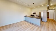 Located on the third floor of a historic building in downtown Kalamazoo, this one-bedroom, one-bathroom unit masterfully blends industrial character with contemporary design. Light hardwood flooring runs throughout, complementing the crisp white walls and clean, modern aesthetic.

The open-concept living, dining, and kitchen area serves as the heart of the unit. A large picture window frames striking views of the surrounding downtown architecture, flooding the space with natural light. The kitchen is well-appointed with dark granite countertops, white shaker-style cabinetry, black hardware accents, stainless steel appliances — including a full-size refrigerator and range — and a dedicated pantry for additional storage. Track lighting overhead adds a modern industrial touch.

A hallway connects the main living area to the private bedroom, which features a dedicated closet and a dramatic exposed brick accent wall that speaks to the building's rich history. The bathroom continues the heritage aesthetic with its own exposed brick wall, complemented by granite counters and modern fixtures. Notably, the bathroom also houses an in-unit washer for added convenience. The entry hallway showcases exposed ductwork, reinforcing the loft-inspired character of the space throughout.