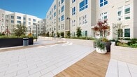 This contemporary residential complex boasts a thoughtfully designed exterior space that seamlessly blends functionality with aesthetics. The courtyard is a standout feature, characterized by a mix of sleek tiled pathways and warm wooden decking. Lush green spaces punctuate the area, providing a refreshing contrast to the building's clean, white facade. 

The complex offers a variety of amenities, including a children's playground with colorful equipment, perfect for young families. Strategically placed planters with trees and shrubs add natural elements throughout the space. For outdoor entertainment, a stainless steel barbecue area is available, ideal for social gatherings.

The building itself showcases modern architecture with large, uniform windows that likely flood the interior spaces with natural light. Stylish light fixtures and carefully curated landscaping enhance the overall ambiance. The design emphasizes communal areas, encouraging resident interaction and fostering a sense of community within the complex.

This well-maintained property combines urban living with green spaces, creating an inviting environment for its residents. The attention to detail in both the landscaping and architectural elements results in a harmonious and attractive living space that caters to various lifestyle needs.