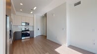 This contemporary single-floor unit offers a thoughtfully designed open-concept layout that seamlessly connects the living area and kitchen. Light wood-tone flooring runs throughout, lending warmth and continuity to the space, while crisp white walls and recessed lighting create a bright, airy atmosphere.

The kitchen is a standout feature, outfitted with stainless steel appliances including a gas range, built-in microwave, dishwasher, and a side-by-side refrigerator. Two-tone cabinetry — combining soft white upper cabinets with sleek grey lower units — pairs with a classic white subway tile backsplash and stone-look countertops, delivering a polished, modern aesthetic. A single-basin sink with a contemporary chrome faucet completes the well-appointed cooking space.

The living area is open and versatile, flooded with natural light and offering a clean canvas for a variety of layouts. A walk-in closet provides generous storage with built-in hanging rods, adding practical functionality to the sleeping area.

The bathroom features a full soaking tub and shower combination enclosed by a sliding glass door, with floor-to-ceiling white subway tile surround. The wood-look flooring extends into the bathroom, maintaining a cohesive design language throughout. The unit is accessed via a private entry door with a smart lock, rounding out a residence that balances modern convenience with clean, contemporary design.