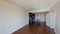 This well-appointed one-bedroom, one-bathroom residence offers a thoughtfully designed open-concept layout finished with rich, dark hardwood flooring throughout the main living areas. The kitchen serves as a central focal point, showcasing dark espresso cabinetry that extends to the ceiling, a mosaic tile backsplash, granite countertops, and a full suite of stainless steel appliances including a gas range, microwave, dishwasher, and refrigerator. A freestanding kitchen island with a warm-toned surface provides additional workspace and casual dining options, illuminated by a trio of pendant lights suspended from a ceiling-mounted track system.

The open living area benefits from expansive floor-to-ceiling windows that invite generous natural light and offer elevated city views. The bedroom continues the hardwood flooring and features large windows with outdoor views, a ceiling fan, and ample natural light. The bathroom is finished with a dual-drawer vanity, white countertop, and tile flooring, and notably includes an in-unit stacked washer and dryer—a practical and convenient feature. The overall aesthetic is contemporary and cohesive, with clean lines and modern finishes throughout.