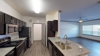 This well-appointed 3-bedroom, 2-bathroom single-story residence offers a thoughtfully designed layout with a blend of modern finishes and comfortable living spaces. The kitchen is a standout feature, showcasing dark espresso cabinetry, granite countertops, a double-basin stainless steel sink, and a full suite of stainless steel appliances including a refrigerator, range, microwave, and dishwasher. Wood-look plank flooring runs through the main living areas, providing a clean and cohesive aesthetic. The living room is generously sized, accented with crown molding, a ceiling fan, and natural light streaming in through large windows with blinds. Each bedroom is carpeted for added comfort, with ceiling fans providing airflow. The primary bedroom includes access to a walk-in closet and an en-suite bathroom featuring granite countertops, a large mirror, and a separate shower. The second bathroom offers a full soaking tub and shower combination with dark cabinetry above. Throughout the home, neutral tones and consistent finishes create a clean, move-in-ready atmosphere suited for a variety of lifestyles.