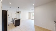 This well-designed 2-bedroom, 2-bathroom single-floor residence offers a thoughtfully laid-out floor plan with modern finishes throughout. The open-concept living and kitchen area serves as the heart of the home, anchored by a central island topped with granite countertops and illuminated by a pair of striking pendant lights. The kitchen is equipped with stainless steel appliances — including a french door refrigerator, electric range, and microwave — complemented by crisp white cabinetry with a subtle tile backsplash. Light hardwood flooring flows seamlessly throughout the entire space, enhancing the bright and airy atmosphere created by recessed lighting and natural light. French doors in the living area provide access to an outdoor area, further opening up the space. Both bedrooms are clean and neutral, with the primary bedroom offering a window view of the surrounding neighborhood. The two bathrooms are finished with granite-topped vanities and warm-toned tile surround — one featuring a soaking tub and shower combination, the other a walk-in shower. The overall aesthetic is clean, contemporary, and move-in ready, making efficient use of the available floor space.