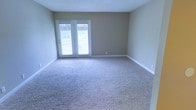 This well-proportioned room offers a blend of comfort and functionality. The space is characterized by its expansive floor area, covered entirely in plush, light-colored wall-to-wall carpeting that adds warmth and comfort underfoot. The room's focal point is a set of elegant French doors, complete with built-in blinds for privacy control, which provide access to an outdoor area and allow natural light to flood the space. Painted in a neutral tone, the walls create a calm, versatile backdrop suitable for various decor styles. The room's simple, clean lines are accentuated by crisp white baseboards and door frames, adding a touch of refinement. With its ample floor space and bright, airy feel, this room offers flexibility for multiple uses, whether as a living area, bedroom, or home office.