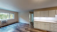 This single-floor unit offers a clean, functional layout with a neutral color palette and thoughtful finishes throughout. The open living and dining area is anchored by warm, wood-look luxury vinyl plank flooring and is bathed in natural light from large windows that frame views of mature trees outside. Baseboard heating runs along the perimeter, ensuring comfort year-round.

The kitchen is efficiently designed with a galley-style configuration, featuring cream-toned cabinetry, light countertops, a stainless steel sink, and white appliances including a gas range, refrigerator, and over-the-range microwave. An extended cabinetry and counter unit connects the kitchen to the living space, offering additional storage and prep or serving space.

The bedrooms are carpeted and quiet, each with generous windows that bring in ample natural light and outdoor views. One bedroom includes a sliding closet door, providing practical storage solutions. The soft, neutral tones of the walls lend a calm and restful atmosphere to these rooms.

The bathroom is well-finished with large-format light-toned tile in the tub surround and on the floor, a soaking tub with a handheld showerhead, chrome grab bars for accessibility, and a vanity topped with a marble-look countertop. The overall design is clean and contemporary, prioritizing both style and function.