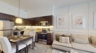 Located at 6161 Southern Blvd in West Palm Beach, Florida, this thoughtfully designed single-floor residence offers a bright and cohesive living experience with a neutral, contemporary aesthetic throughout. The open-concept layout seamlessly connects the kitchen, dining, and living areas, creating a fluid and functional space ideal for everyday living. The kitchen is appointed with rich dark-wood cabinetry, granite countertops, stainless steel appliances including a range, microwave, and refrigerator, and under-cabinet lighting that adds warmth to the space. A dining area sits adjacent to the kitchen, accommodating a full dining table with upholstered seating. The living room is bathed in natural light from a large sliding glass door that opens to the outdoors, featuring light wood-style flooring, wainscoting wall details, and ample space for comfortable seating. The bedroom is a serene retreat highlighted by a textured accent wall, sheer curtains allowing soft natural light, a dedicated workspace with a built-in desk, and access to a walk-in closet. The bathroom is finished with granite countertops, a full tub-shower combination with tile surround, a large vanity mirror, and modern fixtures. Clean lines and a soft, warm color palette unify every room of this well-appointed West Palm Beach residence.