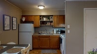 This single-floor residence offers a well-organized and functional layout designed for comfortable everyday living. The kitchen is equipped with warm oak cabinetry, a double-basin sink, a white electric range, and a full-size refrigerator. Open shelving above the counters provides additional storage and display space, while a textured ceiling and flush-mount lighting add a classic touch to the room. Wood-look flooring runs throughout the space, lending warmth and visual continuity from room to room.

The living area is generously proportioned, featuring vertical shiplap-style wall paneling, crown molding, and a ceiling fan that enhances airflow and comfort. A large sofa anchors the space alongside a media console, creating a relaxed and inviting atmosphere. Decorative ladder shelving and wall art contribute to the room's casual, lived-in charm.

The bedroom is a comfortable retreat with a ceiling fan, neutral gray walls, and ample room for a full bed and a dedicated desk area. The bathroom is efficiently laid out with a tub-shower combination, a wood-toned vanity, and a framed mirror.

The entry area features a six-panel front door alongside a window that welcomes natural light into the dining space, where a rustic table and bench provide a welcoming spot for meals.