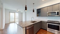 Located at 901 Red River St in the heart of Austin, Texas, this modern single-floor residence offers a thoughtfully designed layout with contemporary finishes throughout. The open-concept kitchen is a standout feature, showcasing gray shaker-style cabinetry — including glass-front upper cabinets — paired with granite countertops, a classic white subway tile backsplash, and warm hardwood flooring. A central island with a undermount sink and stainless steel dishwasher provides additional prep space, while sleek pendant lighting adds a refined touch. The full suite of stainless steel appliances includes a gas range, over-the-range microwave, and a French door refrigerator. The kitchen flows seamlessly into the open living area, which is bathed in natural light from floor-to-ceiling windows offering city views. The bathroom is finished with large-format tile, a soaking tub with shower, a granite-topped vanity, and direct access to a generously sized walk-in closet. The closet is outfitted with a customizable shelving system featuring adjustable shelves, pull-out drawers, and a long countertop surface — offering exceptional storage and organization. An in-unit washer and dryer are also included, adding everyday convenience to this well-appointed urban residence.