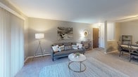 This single-floor residence offers a thoughtfully designed layout that balances comfort and functionality. The living area is generously sized, featuring plush carpeting, neutral gray walls, and a fireplace that serves as a focal point. Large sliding glass doors lead to an outdoor balcony, allowing natural light to fill the room and providing pleasant outdoor views. A separate seating nook adjacent to the living area offers additional flexibility for relaxing or entertaining.

The kitchen is efficiently laid out with dark cabinetry, laminate countertops, and black appliances, including a full-size refrigerator. Tile flooring runs throughout the kitchen, and a breakfast bar provides a convenient casual dining surface. The adjacent dining area accommodates a full dining set, making the space well-suited for everyday meals.

The bedroom is a calm, carpeted retreat with ample room for a large bed and additional seating. A walk-in closet offers generous storage, and a window provides natural light. The full bathroom features a wide vanity with a large mirror, tile flooring, and a shower-tub combination, all finished in coordinating neutral tones.

Throughout the space, a consistent palette of warm grays and soft neutrals creates a cohesive and inviting ambiance, while baseboard heating is present in multiple rooms for year-round comfort.