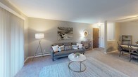 This single-floor residence offers a thoughtfully designed layout that balances comfort and functionality. The living area is generously sized, featuring plush carpeting, neutral gray walls, and a fireplace that serves as a focal point. Large sliding glass doors lead to an outdoor balcony, allowing natural light to fill the room and providing pleasant outdoor views. A separate seating nook adjacent to the living area offers additional flexibility for relaxing or entertaining.

The kitchen is efficiently laid out with dark cabinetry, laminate countertops, and black appliances, including a full-size refrigerator. Tile flooring runs throughout the kitchen, and a breakfast bar provides a convenient casual dining surface. The adjacent dining area accommodates a full dining set, making the space well-suited for everyday meals.

The bedroom is a calm, carpeted retreat with ample room for a large bed and additional seating. A walk-in closet offers generous storage, and a window provides natural light. The full bathroom features a wide vanity with a large mirror, tile flooring, and a shower-tub combination, all finished in coordinating neutral tones.

Throughout the space, a consistent palette of warm grays and soft neutrals creates a cohesive and inviting ambiance, while baseboard heating is present in multiple rooms for year-round comfort.