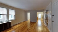 Located at 117 North Essex Avenue in the charming borough of Narberth, Pennsylvania, this single-floor residence offers a clean, functional layout with timeless finishes. The main living area is generously proportioned, showcasing warm-toned hardwood floors that extend throughout the space, lending a classic and inviting character to the interior. Neutral-painted walls complement the natural light that streams in through multiple windows fitted with blinds, creating a bright and airy atmosphere. The open sightlines from the living area connect seamlessly to adjacent rooms, offering a sense of continuity and flow. A doorway leads to what appears to be a private room or hallway, while a passage toward the rear of the space opens to a kitchen area illuminated by natural light from a rear-facing window. Additional access is provided through a glass-paneled door, adding architectural interest and further enhancing the light within the space. Baseboard heating is present throughout, ensuring year-round comfort. The overall ambiance is understated and functional, with hardwood flooring and classic millwork providing a solid foundation for a variety of living arrangements. The residence benefits from its location in Narberth, a walkable and well-regarded community in the Philadelphia suburbs.