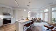 Located at 2925 Buford Dr in Buford, GA, this single-floor residence offers a thoughtfully designed open-concept layout with modern finishes and an inviting ambiance throughout. The kitchen serves as a central hub, featuring gray shaker-style cabinetry, a classic subway tile backsplash, stainless steel appliances, and a generous island with a white quartz countertop and bar seating — ideal for casual dining or entertaining. Pendant lighting and a track light system illuminate the space with both style and practicality. Rich hardwood-style flooring flows seamlessly from the kitchen into the living area, which is anchored by a tray ceiling with crown molding and floor-to-ceiling windows that invite abundant natural light and outdoor views. The bedrooms are carpeted for comfort and feature large windows, ceiling fans, and ample closet space, including a spacious walk-in closet with built-in shelving and wire organizers. The bathroom is well-finished with tile-surround tub and shower, white vanity with quartz countertop, and wood-tone flooring. Overall, the space balances clean, contemporary design with warm, functional details throughout every room.