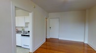 This single-floor residence offers a straightforward and functional layout with a clean, understated aesthetic. The main living area is highlighted by rich hardwood flooring that adds warmth and character to the space, complemented by smooth white walls and simple baseboards that contribute to a bright, airy atmosphere. A white-paneled entry door anchors one end of the living area, providing a welcoming focal point.

Adjacent to the living area, the kitchen is efficiently arranged and features white cabinetry providing ample storage, a gas range, and countertops that offer practical workspace. The open pass-through between the kitchen and living area enhances the sense of connection and flow throughout the home.

The overall design is minimal and neutral, making it a versatile canvas well-suited to a variety of furnishing styles and personal tastes. The light-toned walls reflect natural and ambient light effectively, keeping the interior feeling open and uncluttered. The consistent use of white trim and doors throughout ties the space together cohesively. This residence offers a practical and comfortable living environment with classic details like hardwood flooring that provide lasting appeal.