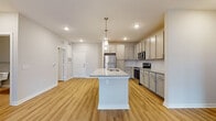 This well-appointed single-floor residence in Morganton, NC offers a clean, modern aesthetic throughout. The open-concept kitchen serves as the heart of the home, featuring grey shaker-style cabinetry with gold hardware, a white subway tile backsplash, granite countertops, stainless steel appliances, and a central island with a built-in sink — all illuminated by pendant lighting and recessed fixtures over warm-toned hardwood-style flooring. The living area extends naturally from the kitchen, offering a ceiling fan, abundant natural light, and access to an exterior door. The bedrooms are carpeted for comfort, each equipped with ceiling fans and windows that bring in natural light. The primary bathroom is well-appointed with a glass-enclosed shower, a granite-topped vanity with grey cabinetry, and direct access to a walk-in closet. A secondary bathroom includes a soaking tub with a shower surround and safety grab bars. A dedicated laundry room houses a full-sized washer and dryer. Neutral wall tones and consistent finishes create a cohesive, move-in-ready environment throughout the home.