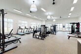 Located at 560 Jack Clift Blvd in Madison, Alabama, this generously sized fitness center offers a comprehensive exercise environment across a single, open floor. The space is designed with a clean, modern aesthetic, featuring crisp white walls, speckled rubberized flooring, and a combination of recessed linear lighting and stylish pendant fixtures that ensure bright, even illumination throughout.

Large windows along multiple walls flood the space with natural light and provide views of the surrounding community, creating an open and motivating atmosphere. Ceiling fans are distributed throughout to enhance airflow and comfort during workouts.

The main exercise area is thoughtfully arranged with a robust selection of equipment. Cardio machines include multiple treadmills, ellipticals, a stair climber, and a rowing machine, while strength training is well supported by cable machines, a multi-functional rack, a full dumbbell rack, and adjustable benches. A dedicated alcove area features a spin bike, a rowing machine, and wall-mounted flat-screen televisions, ideal for focused or instructor-led sessions.

A built-in storage wall with dark wood cabinetry, shelving, and coat hooks adds a functional and polished finishing touch near the entryway. Steel-framed glass partitions contribute an industrial-modern design element, tying the overall aesthetic together seamlessly.