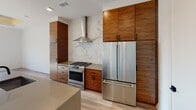 This thoughtfully renovated single-floor residence showcases a seamless blend of modern design and high-quality craftsmanship throughout its open layout. The kitchen is a standout feature, equipped with rich, warm-toned wood cabinetry that extends floor to ceiling, a striking marble slab backsplash with bold veining, stainless steel appliances including a gas range and French door refrigerator, and a stainless steel wall-mounted range hood. Light wood flooring runs throughout, complementing the warm tones of the cabinetry and creating a cohesive aesthetic.

The living area benefits from large, multi-pane black-framed windows that invite generous natural light and offer views of the surrounding cityscape. A distinctive tray ceiling with recessed detailing adds architectural interest and visual depth to the room.

The bathroom is elegantly appointed with subway tile walls, dark slate-toned floor tiles, a wide double-sink vanity set on a warm wood base with matte black hardware, a large framed mirror, and a freestanding soaking tub visible in the background. Clean white surfaces are balanced by bold black fixtures, creating a sophisticated, spa-like atmosphere. Built-in cabinetry provides ample storage. Every detail of this space reflects careful attention to modern design and functional living.