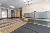 Located at 130 Rosedale Valley Rd in Toronto's prestigious Rosedale neighbourhood, this building lobby offers a refined and welcoming first impression. The space is finished with polished granite flooring and warm marble-toned wall cladding throughout, lending an air of classic elegance. A grand chandelier anchors the main entry area, which is bathed in natural light from large glass automatic doors that frame views of the surrounding greenery.

The lobby is organized across two levels connected by granite-clad stairs with sleek stainless steel railings. At the upper level, two textured stainless steel elevator doors provide access to the building's residences, set against a backdrop of polished stone columns and tile. A row of individual mailboxes lines one wall near the entrance, alongside a parcel locker station for resident convenience.

A glass-partitioned lounge area features rich burgundy leather Chesterfield seating and curated artwork, offering a sophisticated retreat within the lobby. Adjacent to this is a fully furnished reading room, appointed with dark wood bookshelves stocked with books, a leather executive chair, and comfortable seating arranged around a coffee table — ideal for quiet study or relaxed conversation. Together, these spaces create a polished, community-oriented atmosphere that reflects the character of this distinguished Toronto address.