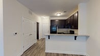 This single-story, one-bedroom, one-bathroom residence offers a thoughtfully designed layout that maximizes functionality and comfort. The open-concept living and kitchen area is anchored by durable wood-style plank flooring that runs throughout the main living spaces, creating a cohesive and modern aesthetic. A ceiling fan with integrated lighting in the living area adds both comfort and practicality, while a glazed door allows natural light to filter in.

The kitchen is a standout feature, equipped with rich dark espresso cabinetry that extends to the ceiling for ample storage. Black appliances — including a refrigerator, electric range, and over-the-range microwave — complement the cabinetry, while granite-style countertops add a polished finish. A peninsula with an overhang provides convenient bar seating and defines the transition between the kitchen and living area.

The bedroom is finished with plush neutral carpeting and features a window with blinds that brings in natural light. A ceiling fan enhances the room's comfort. The bathroom includes a full tub-shower combination, a dark vanity with a granite-style countertop, a large mirror, and wood-style flooring. Generous closet space is also present near the entryway, adding to the unit's overall storage capacity.