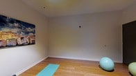 This single-floor wellness space is designed to serve as a dedicated area for physical activity and mindful exercise. The room features warm hardwood flooring that provides a clean, supportive surface well-suited for yoga, stretching routines, and general fitness activities. The floors are complemented by smooth, neutral-toned walls finished in a soft gray palette, creating a calm and focused atmosphere conducive to exercise and relaxation.

The open layout of the room allows for unrestricted movement, making it versatile for a range of fitness disciplines. A teal yoga mat is positioned on the floor, and a stability ball rests nearby, indicating the room's primary use as a personal fitness studio. The wall space is largely unobstructed, offering room for wall-mounted accessories or additional equipment as needed. A colorful wall art piece adds a subtle visual accent without overwhelming the minimalist aesthetic.

The ceiling is smooth and adequately elevated, contributing to an open, airy feel. Overall, the space presents a clean, purposeful environment optimized for personal wellness activities.